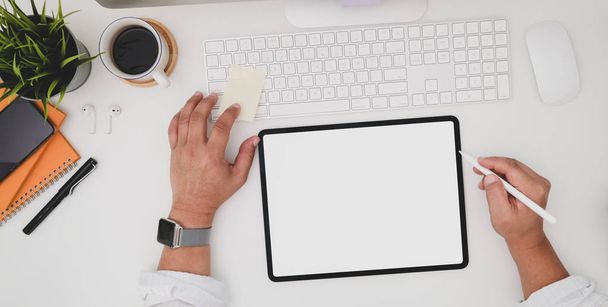 Vista superior de un joven hombre de negocios escribiendo en una tableta de pantalla en blanco en una moderna sala de oficina con suministros de oficina
  - Foto, imagen
