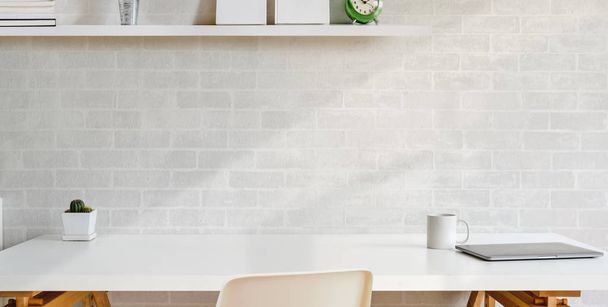 Oříznutý záběr pohodlného pracoviště s kancelářskými poskvrnami na dřevěném stole a bílou cihlovou stěnou pozadí  - Fotografie, Obrázek
