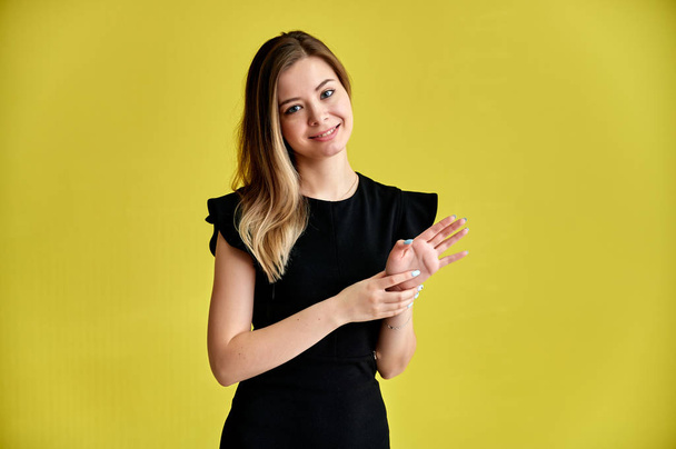 Portrait of a pretty young smiling girl on a yellow background in a black dress with long straight hair. Standing right in front of the camera, Shows emotions, talks in different poses. - Фото, зображення