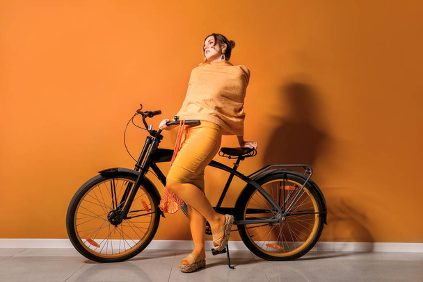 Mujer joven de moda con bicicleta cerca de la pared de color
 - Foto, imagen