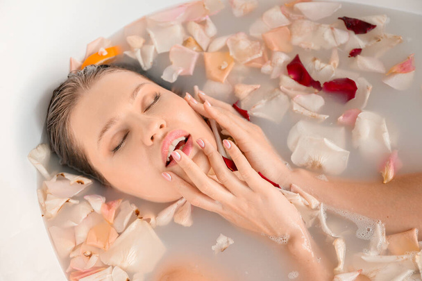 Beautiful young woman taking bath with flower petals at home - Foto, imagen