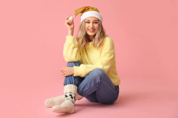 Happy young woman in winter clothes and Santa Claus hat on color background - Fotó, kép