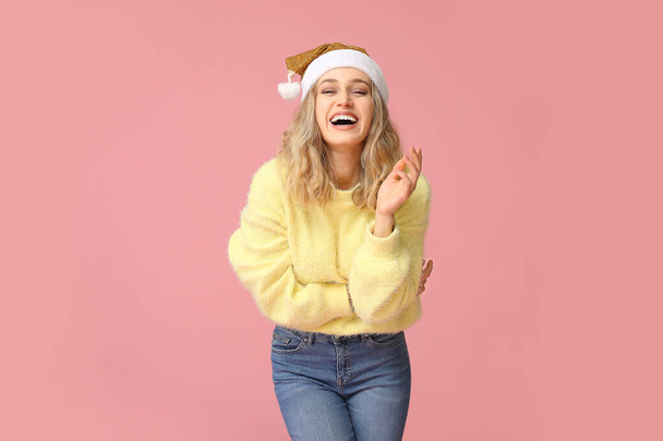 Šťastná mladá žena v zimním oblečení a Santa Claus klobouk na barevném pozadí - Fotografie, Obrázek