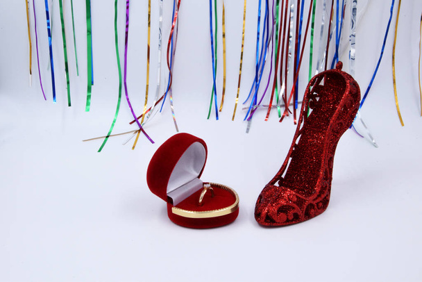 Fehér háttér - egy élénk piros női cipő sarokkal és egy jegygyűrű egy piros bársony dobozban. Női kedvenc dolgok gyűrű és magas sarkú cipő. - Fotó, kép