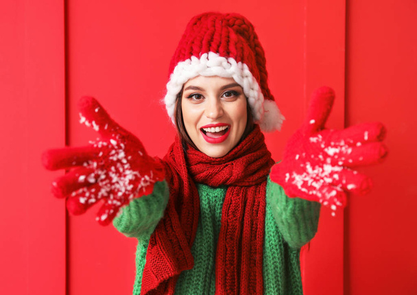 Beautiful young woman in Santa hat playing with snow on color background - Photo, Image
