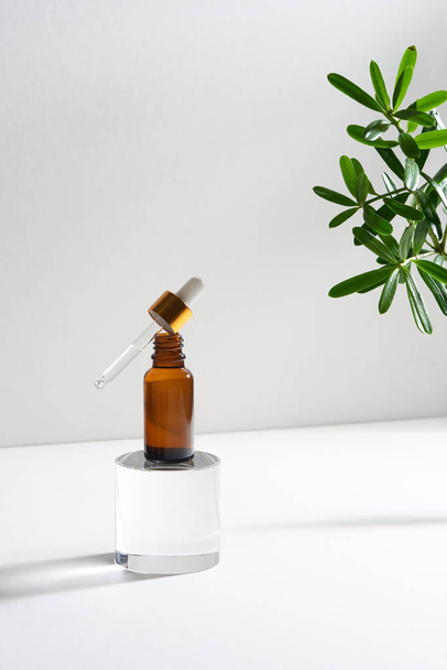 Serum or essential oil bottle isolated on with background with green leaves. Beauty product concept. - Photo, Image