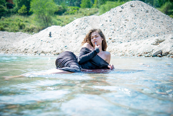 young romantic woman in wet dress lying in river on sand quarry background - Foto, afbeelding