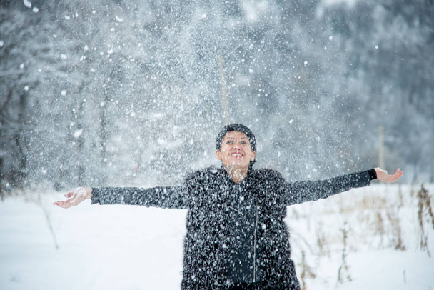 happy smiling brunet woman throwing up snow on winter wood background  - Φωτογραφία, εικόνα