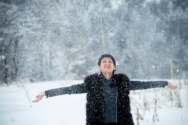 happy smiling brunet woman throwing up snow on winter wood background  - Fotoğraf, Görsel