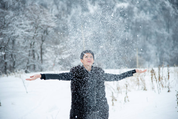 happy smiling brunet woman throwing up snow on winter wood background  - Фото, изображение