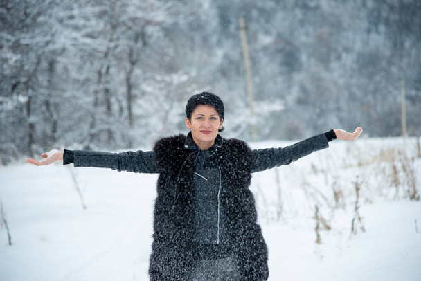 brunet woman in black fur vest standing in winter wood background - Valokuva, kuva
