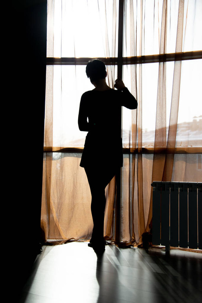 woman model silhouette standing with brown curtains in the windows room - Fotó, kép