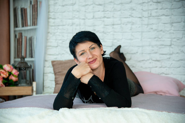 woman brunet in black jumper lying on bed in photo studio - Fotoğraf, Görsel