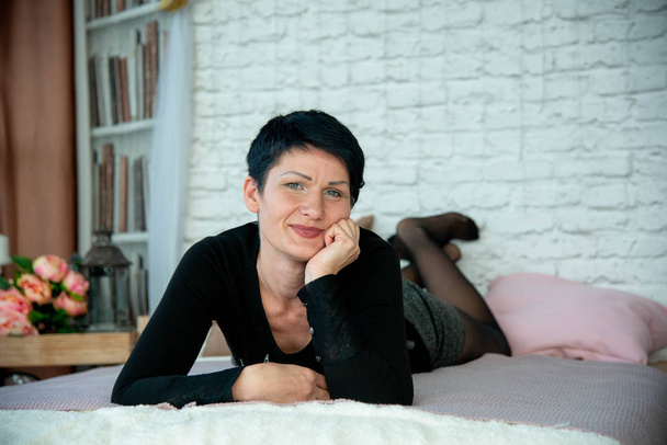woman brunet in black jumper lying on bed in photo studio - Fotoğraf, Görsel