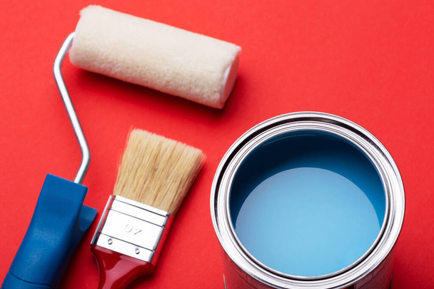 Can of blue paint, paint roller and brushe on red. - Photo, Image