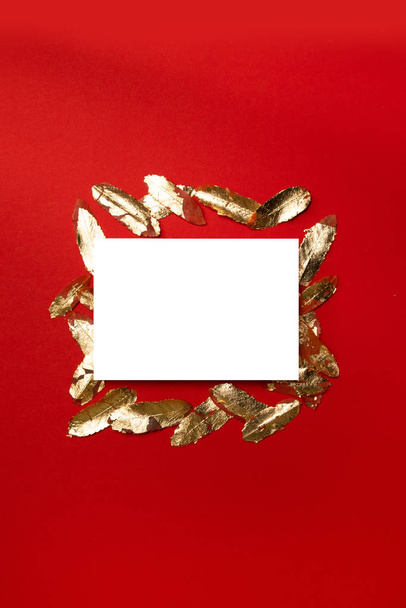 Δημιουργική κάθετη σύνθεση με λευκό λευκό λευκό υπόδειγμα καρτ ποστάλ με φύλλα χρυσού σε κόκκινο φόντο. - Φωτογραφία, εικόνα