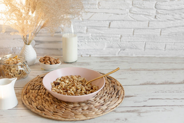 Granola s rozinkami a lískovými oříšky podávaná s mandlovým mlékem na dřevěném stole. Zdravá snídaně. - Fotografie, Obrázek