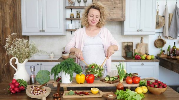 Mulher grávida feliz cozinhar salada saudável na cozinha
. - Foto, Imagem