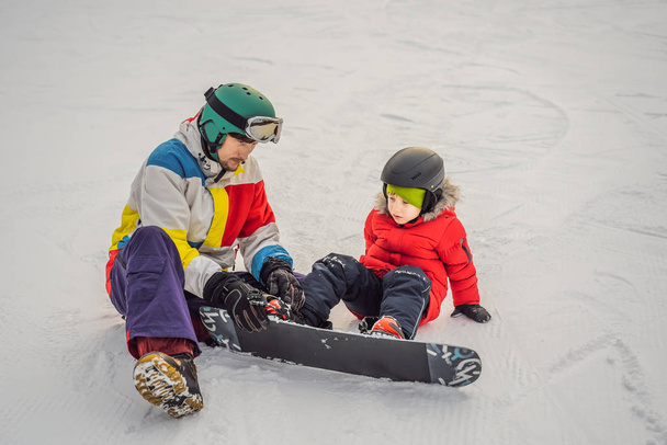Snowboard instructor teaches a boy to snowboarding. Activities for children in winter. Childrens winter sport. Lifestyle - 写真・画像