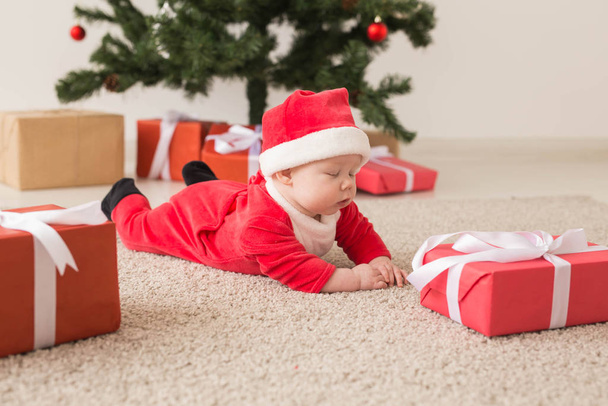 Cute baby girl wearing santa claus suit crawling on floor over Christmas tree. Holiday season. - 写真・画像