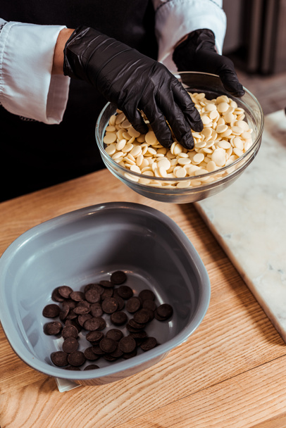 abgeschnittene Ansicht eines Chocolatiers, der weiße Schokoladenchips in Schüssel gibt  - Foto, Bild