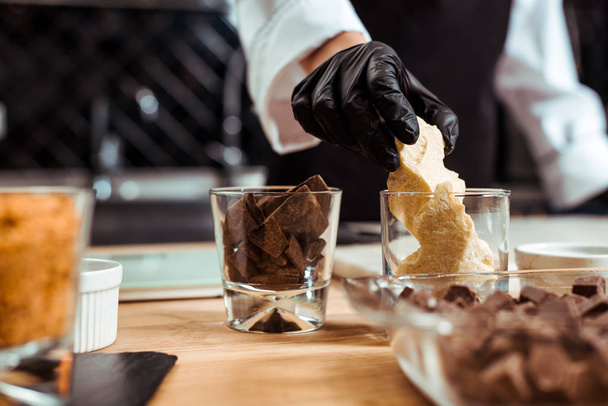 cropped view of chocolatier taking white chocolate from glass in kitchen   - Foto, afbeelding