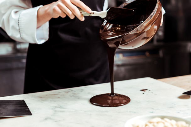 bijgesneden weergave van chocolatier gieten gesmolten chocolade op marmeren oppervlak  - Foto, afbeelding