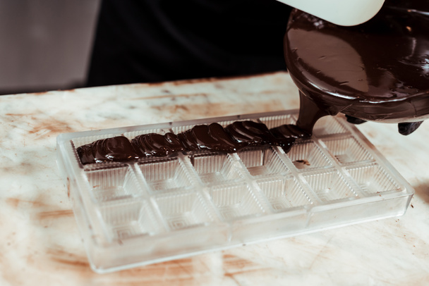 cropped view of chocolatier pouring melted chocolate into ice tray  - Foto, afbeelding