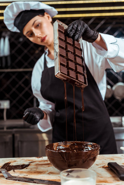 selektywne skupienie atrakcyjnej czekolady w fartuchu trzymającym tacę z lodem ze stopioną czekoladą w pobliżu miski  - Zdjęcie, obraz