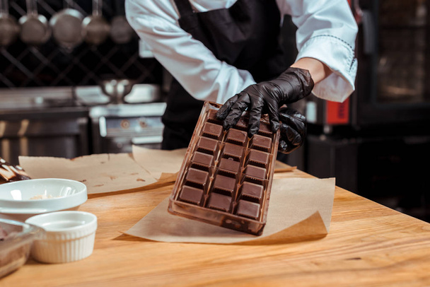 vista recortada del chocolatero sosteniendo bandeja de hielo con chocolate cerca de papel de hornear
  - Foto, Imagen