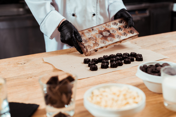 foco selectivo del chocolatero sosteniendo bandeja de hielo cerca de dulces de chocolate preparados en papel de hornear
  - Foto, Imagen