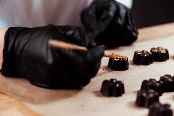 cropped view of chocolatier holding brush near prepared chocolate candies  - Foto, afbeelding