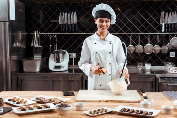 happy chocolatier in chef hat holding cooking thermometer near bowl with melted white chocolate  - Photo, Image