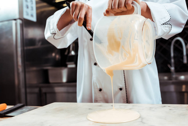 cropped view of chocolatier with spatula pouring melted white chocolate on marble surface  - Photo, Image