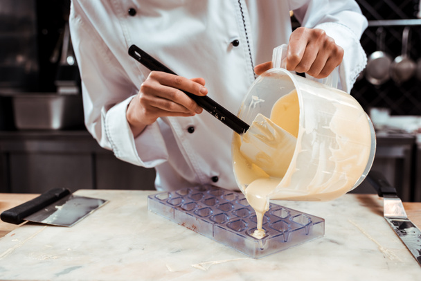 cropped view of chocolatier pouring melted white chocolate into ice tray  - Fotografie, Obrázek