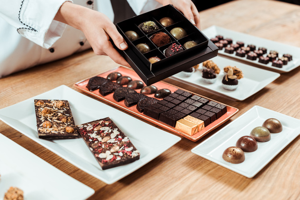 cropped view of chocolatier holding box with tasty and fresh made chocolate candies  - Fotografie, Obrázek