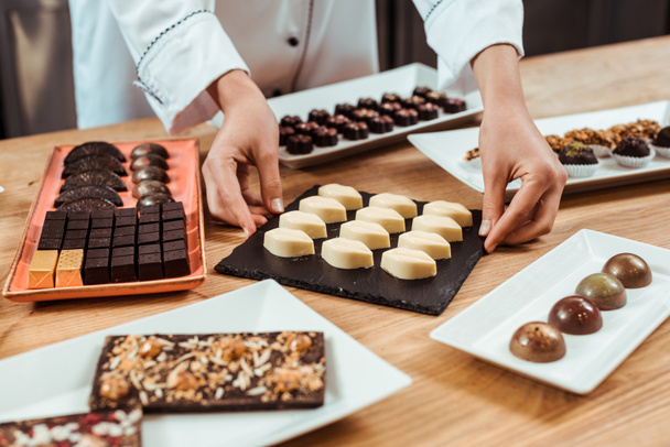 cropped view of chocolatier touching plate with tasty white chocolate candies  - Photo, Image