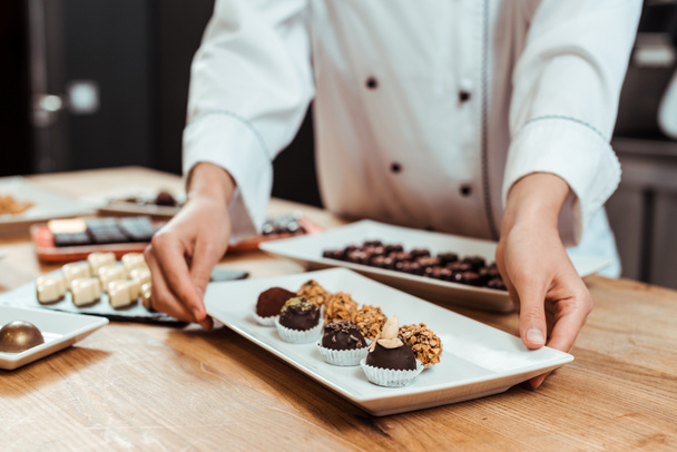 cropped view of chocolatier touching plate with sweet fresh chocolate candies  - Φωτογραφία, εικόνα