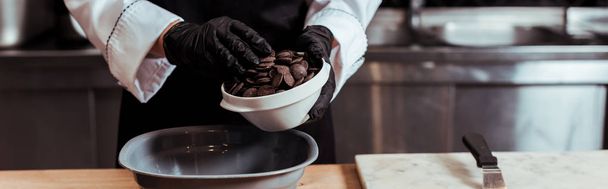 Colpo panoramico di cioccolatiere in guanti di lattice aggiungendo gocce di cioccolato fondente nella ciotola
  - Foto, immagini
