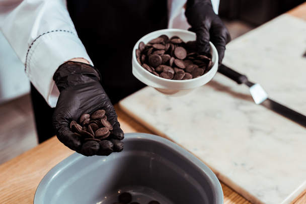 cropped view of chocolatier holing dark chocolate chips in hand - Fotó, kép