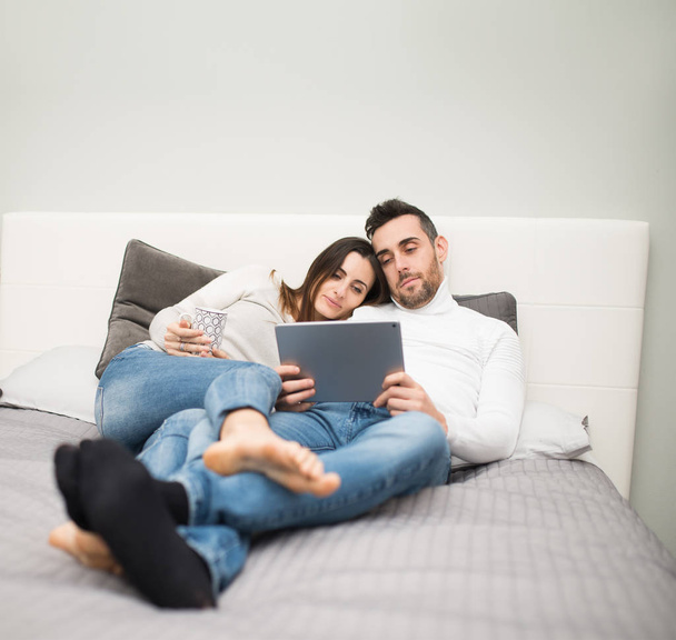 Jeune couple regardant un film sur leur tablette pendant qu'ils sont sur le lit
 - Photo, image
