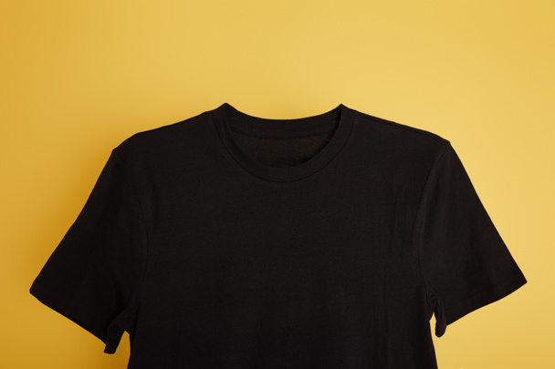 top view of basic black t-shirt on yellow background - Foto, Imagen