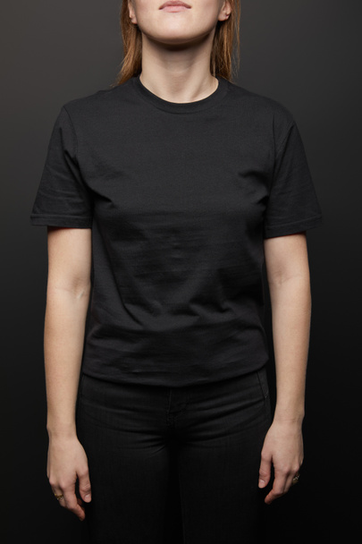 przycięty widok kobiety w pusty podstawowy czarny t-shirt na czarnym tle - Zdjęcie, obraz