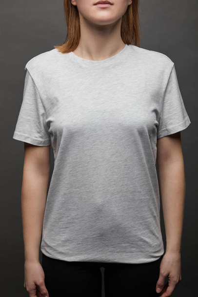 cropped view of woman in blank basic grey t-shirt on black background - Φωτογραφία, εικόνα