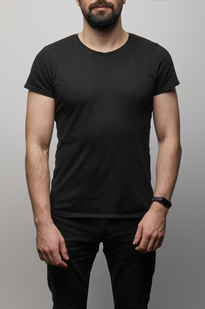 cropped view of bearded man in blank basic black t-shirt on grey background - Fotoğraf, Görsel