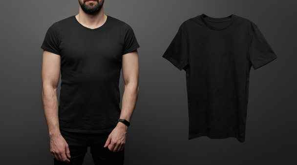 cropped view of bearded man near blank basic black t-shirt on black background - Foto, imagen