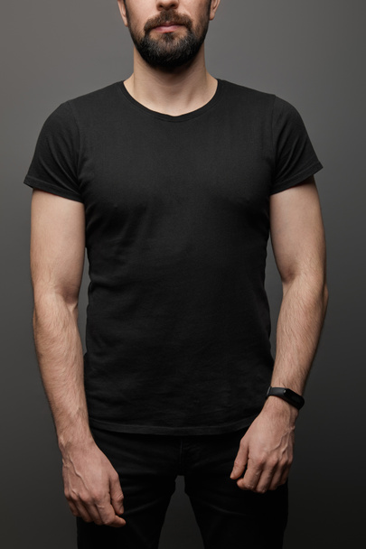 cropped view of bearded man in blank basic black t-shirt on black background - Foto, afbeelding