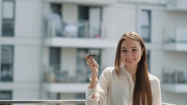 Frau winkt Autoschlüssel in der Hand und lächelt auf Balkon - Filmmaterial, Video