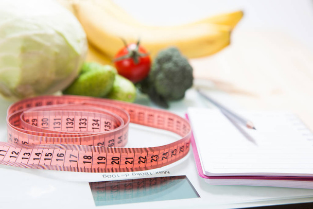 The concept of a healthy diet, fitness and weight loss. Fruits, vegetables, scales, measuring tape on the table. - 写真・画像