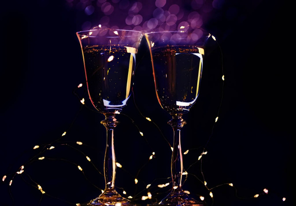Two glasses with champagne sparkling wine on a dark background and sparkling bokeh. Atmosphere of celebration, magic and happiness. - 写真・画像